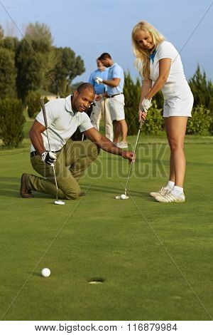 Golf instructor teaching pretty golfer to putt.
