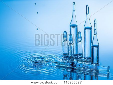 Medical ampoules and syringe on blue water background with splash and drops