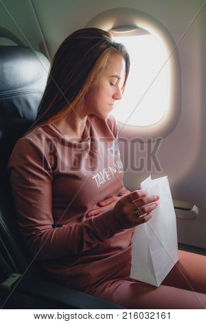 Girl is sick in the airplane and seating with paper pocket