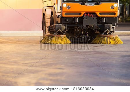 Yellow urban sweeper cleans road from dirt with a round brush