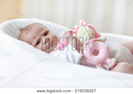 Cute adorable newborn baby playing with pink plush animal rattle toy. in white bed at home. New born child, little girl looking surprised at the camera. Family, new life, childhood, beginning concept