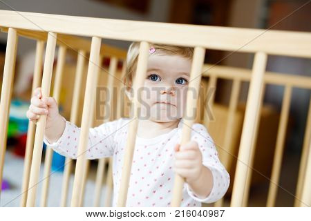 Beautiful little baby girl standing inside playpen. Cute adorable child playing with colorful toys. Home or nursery, safety for kids.