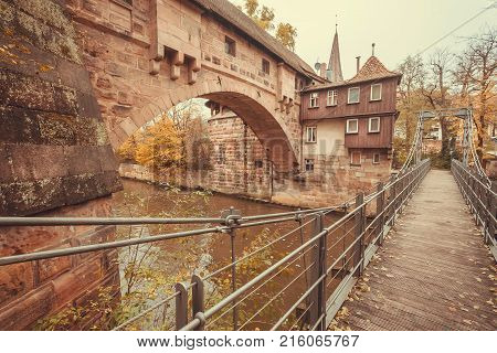 Stone houses and suspension bridge across the river in the historic city of Nuremberg with historical walls. Old Bavaria of Germany.