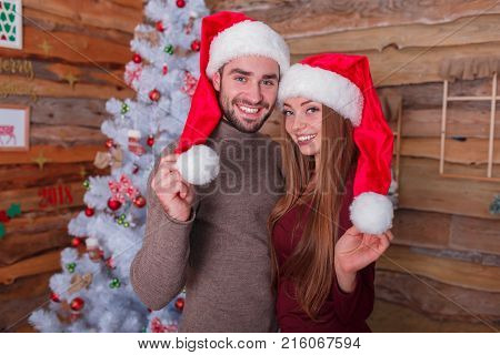 A guy with a girl is fucking in New Year's hat standing together. Hold the tips of New Year's hats against the backdrop of a smart Christmas tree