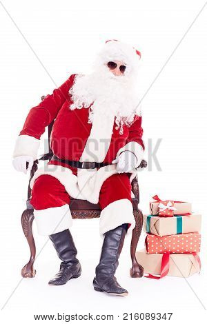 Portrait of swaggy Santa Claus in sunglasses relaxing in chair on white background
