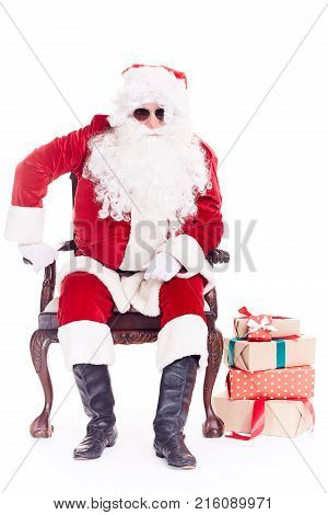 Portrait of swaggy Santa Claus in sunglasses relaxing in chair on white background