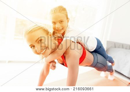 Mother and daughter are engaged in yoga in sportswear. They are in a bright room with panoramic windows. They in kumbhakasana asana, plank pose.
