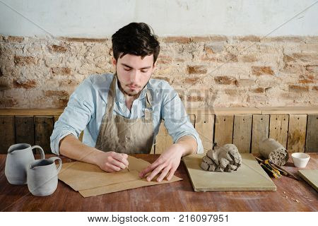 Handsome Young Mexican Potter Does Sketches Of Ceramics On The Paper. Concept Of Small Business Hand