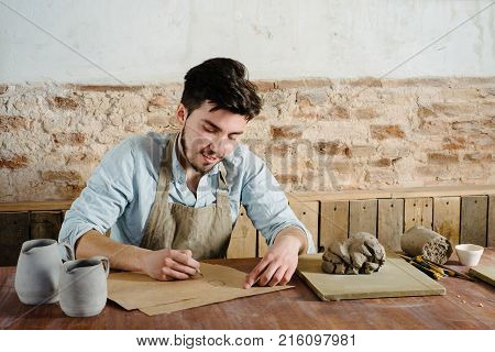 The Smiling Handsome Young Mexican Potter Does Sketches Of Ceramics On The Paper. Concept Of Small B
