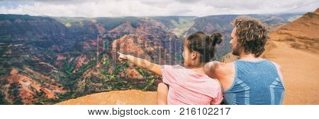 People hiking in Hawaii banner hikers pointing at Kauai mountains. happy hiker couple healthy lifestyle outdoors looking at Waimea canyon view. Young couple in nature in Kauai, Hawaii, USA.