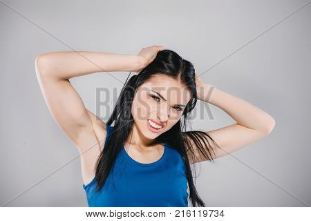 young woman with long brunette hair in blue dress giving angry emotion in photostudio on gray background