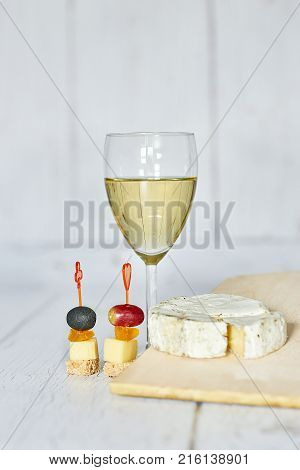 Glass of white wine, canapes and camembert cheese on a wooden background - vertica