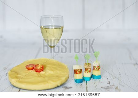 Glass of white wine, polenta with cherry tomato and chese canapes on a wooden background