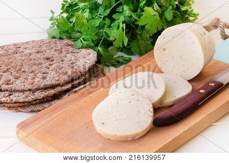 Dietary homemade boiled sausage mortadella from chicken breast with spices on a wooden cutting board. Protein rye multicereal flatbread. White background.