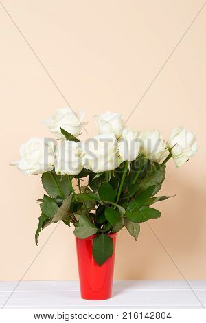 white roses in red vase on bege background