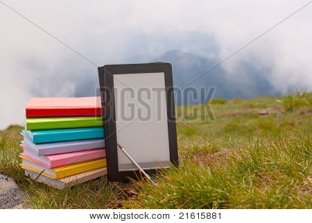 Pile de livres colorés et de lecteur de livre électronique sur l'herbe