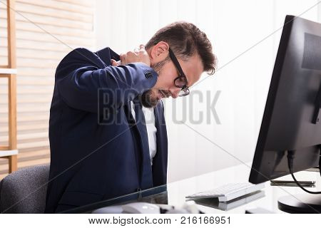 Young Businessman Sitting In Office Suffering From Neckache