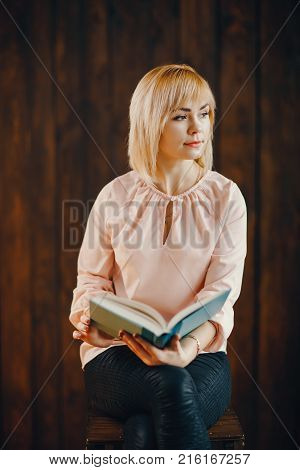 blonde girl sitting on a chair and reading a book