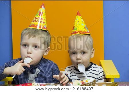 Children in funny caps eat on holiday.Birthday party. Brothers celebrate the holiday. Children at the festival eat. Festive food.Children's parties and entertainment