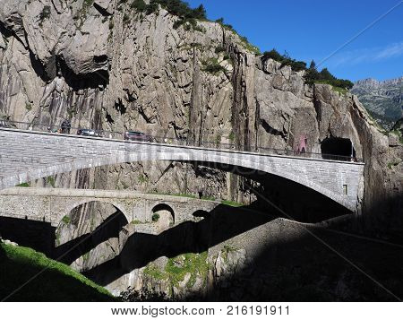 St. Gotthard and Teufelsbruecke, alpine Devil's road bridge and tunnel over Reuss river near Andermatt town in Switzerland, rocky mountains landscape scenery in 2017 warm summer day, Europe on July.