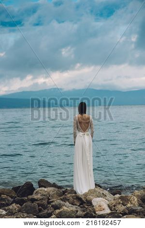 Beautiful Bride standing by the Sea. Destination wedding concept. Wedding on exotic island. Bride in white wedding dress watching sea. 