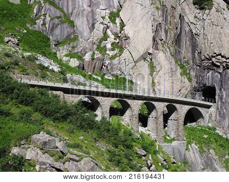 Scenic stony rail bridge in swiss Alps in SWITZERLAND near Andermatt town with alpine rocky mountains landscape scenery in 2017 warm summer day, Europe on July.