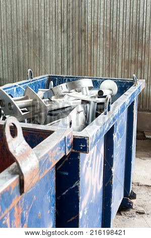 Waster metallic container bin with full with rubbish on factory in workshop. Vertical colored image.