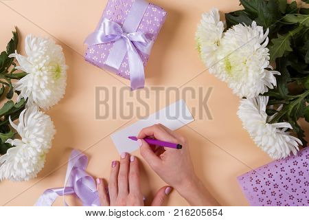 woman hand writing a note with the text thank you on a paper, over beige table and flowers