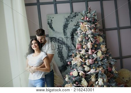 Beautiful young couple in love decorating Christmas tree, arranging the christmas lights and having fun