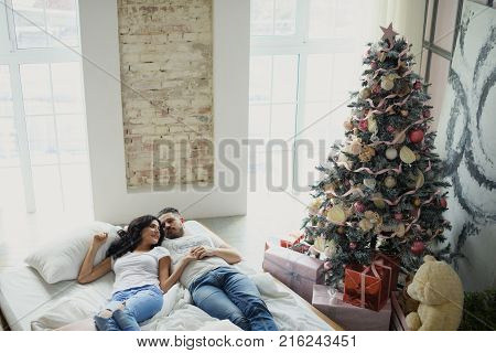 Beautiful young couple in love decorating Christmas tree, arranging the christmas lights and having fun