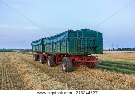 Green Agriculture trailer covered with a tarp, loaded with harvest. At sunset