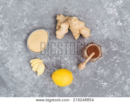 Top view of ginger slice, ginger root, ginder powder, lemon and honey on gray concrete background. Healthy food concept