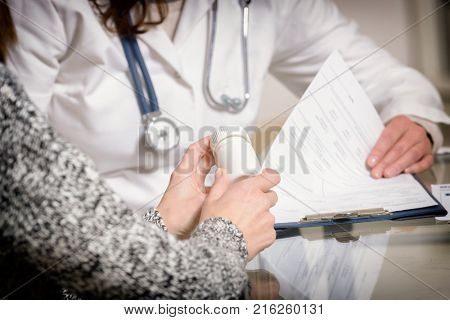 Patient holding a bottle of pills and doctor making notes in background