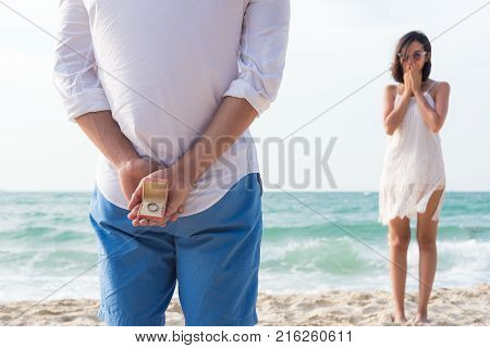 man making proposal with engagement ring and gift box to his woman at sea beach - wedding concept