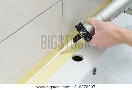 A man is puting the silicone sealant to caulk the joint between a washbasin and a wall.
