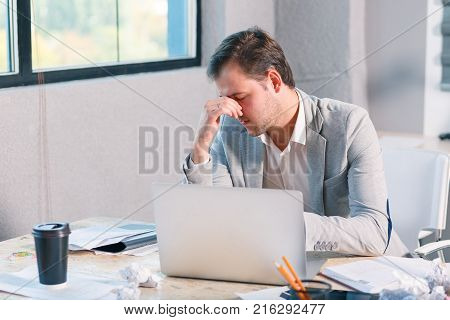 A frustrated man, an office worker works behind a laptop, because of problems he is frustrated holding his head. Inside the office.