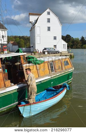 WOODBRIDGE, SUFFOLK, ENGLAND - APRIL 17, 2017: Man doing boat repairs at Woodbridge Quay with tide mill in the background.