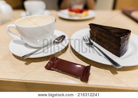 A piece of traditional austrian sachertorte on plate on wooden background. Chocolate cake and a cup of coffee. Closeup shot.