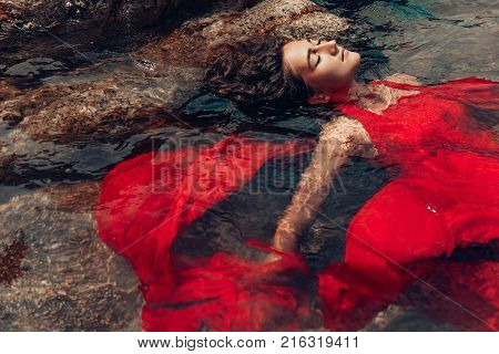 beautiful young woman in red dress laying dowm in water