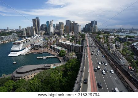 SYDNEY AUSTRALIA - NOVEMBER 24 2017; Vehicles cruise along Cahill Highway that projects straight ahead into distance and city skyline with large cruise ship moored at Circular Quay Australia