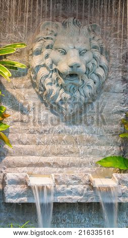 Statue marble lion on stone wall and waterfall in cozy garden.