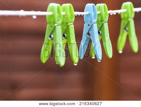 conceptual image of a rainy day seletcive focus on a blue wet peg dripping raindrops in the yard bokeh background to accomated text overlay and copy space