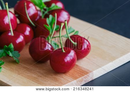 Close up fresh cherries on wood cutting board. Red cherry put on black granite table in side view with copy space. Cherry have high vitamin C and have sweet and sour taste. Healthy friut concept of red cherry. Delicious and sweet cherry.