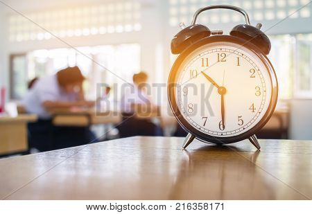 Closeup of Retro alarm clock with ten o'clock on table teacher in blur students exams classroom. Time is indefinite continued progress of existence. Education concept selective focus.