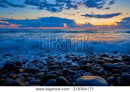 Beautiful sunset with blue wave and moist stones