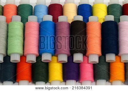 Background with a lot of colorful coils with threads. Bobbins are stacked in three rows one on the other. The winding is erratic. Multicolored threads.