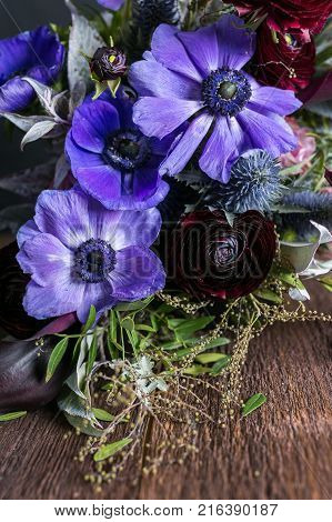 nature, flower arranging, hobby concept. close up of great lilac anemons with puffy black centers that placed in the bouquet decorated with various leaves and battercups