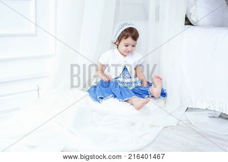 Funny and cute brunette little smiling girl sits on fluffy carpet in bright room