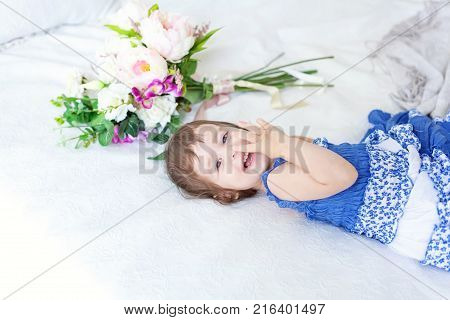 Funny and cute brunette little smiling girl playing on bed in bedroom. White interior with big bed