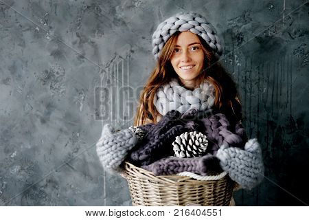 Winter fashion accessories.Young woman dressed for cold weather in grey snood hat and mittens holding a basket full of knitted clothes.